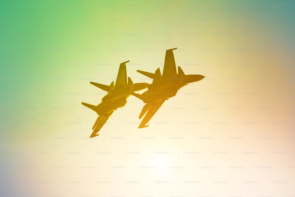 두 개의 항공기 전투기 제트 비행기 태양 광선 따뜻한 노란색 주황색 녹색 그라데이션 하늘.