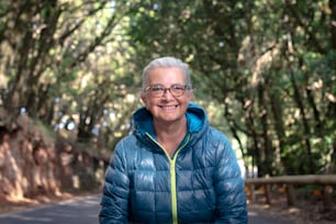Mujer mayor alegre y sonriente con cabello blanco y anteojos que disfruta de la libertad y la naturaleza en una excursión en el bosque