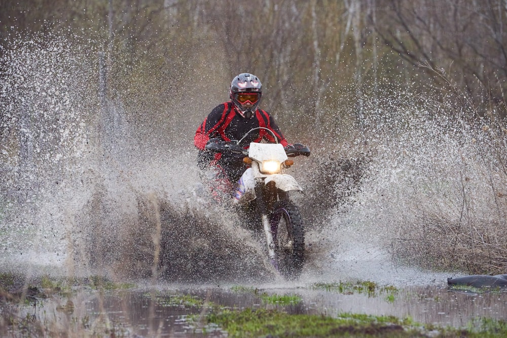 Pilote de motocross faisant la course dans les bois inondés et éclaboussant une grande flaque d’eau à grande vitesse