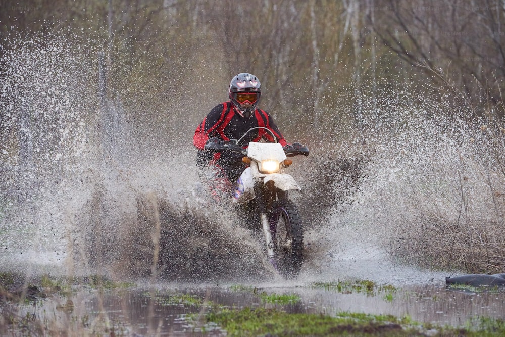 Motorcross rider racing in flooded wood and splashing big puddle on high speed