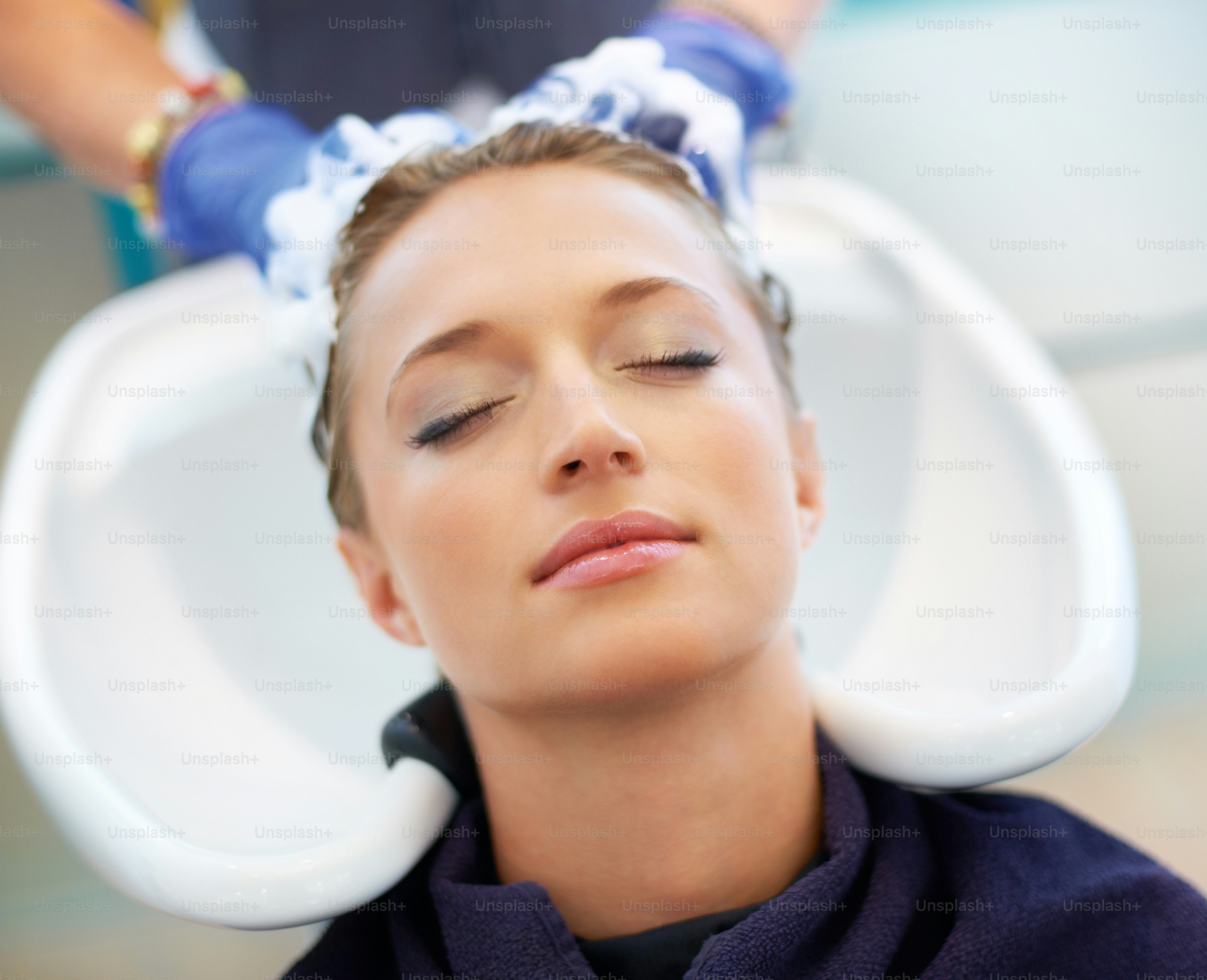 Schöne junge Frau, die sich zurücklehnt und sich im Salon die Haare waschen lässt