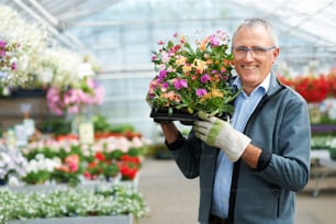 Un homme tenant un plateau de fleurs dans une serre