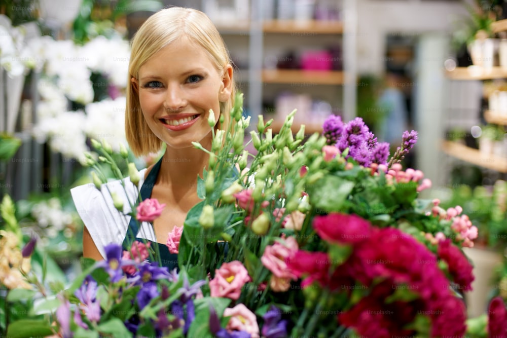 Cute young florist holding an armful of fresh flowers with a smile