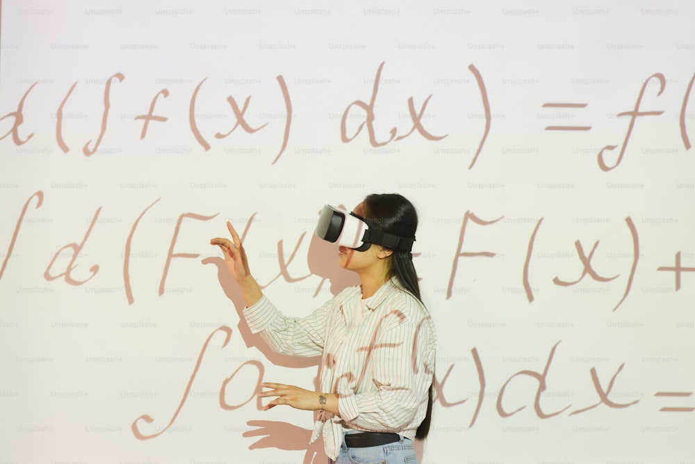 Brunette student girl in virtual reality headset pointing at projection screen while working with math equation