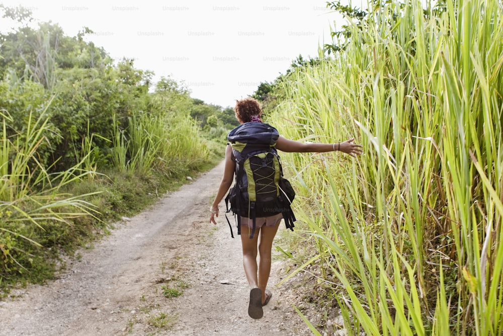 a woman walking down a dirt road next to tall grass