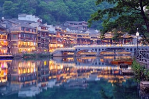 Destino de atracción turística china: la ciudad antigua de Feng Huang (ciudad antigua de Phoenix) en el río Tuo Jiang con el puente iluminado por la noche. Provincia de Hunan, China