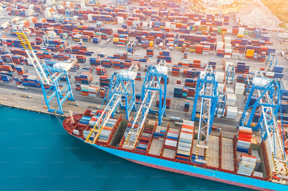 Aerial top view - heavy huge ship with a lot of containers moored at the pier in the port, loading with cranes in the industrial port