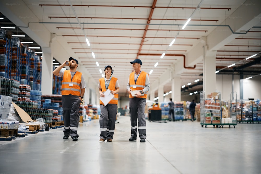 Employée d’entrepôt heureuse et ses collègues masculins marchant dans l’entrepôt de distribution. Espace de copie.