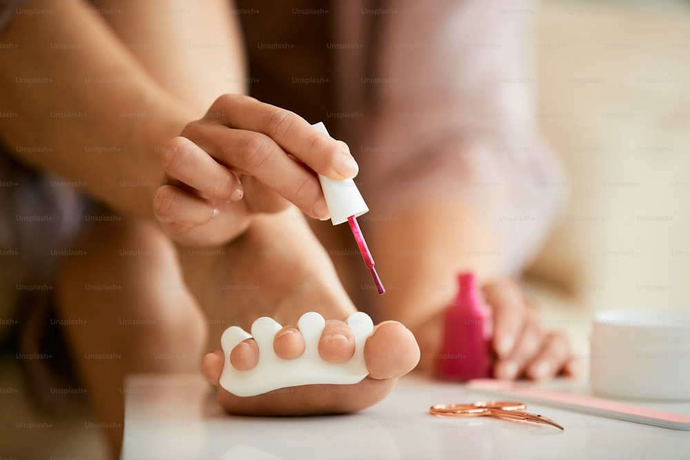 Close-up of woman applying nail polish on her toenails at home.