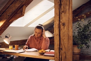 Young woman listening music over headphones while studying at home.