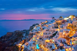 Famoso punto iconico greco per selfie destinazione turistica Villaggio di Oia con le tradizionali case bianche e mulini a vento nell'isola di Santorini nell'ora blu serale, Grecia