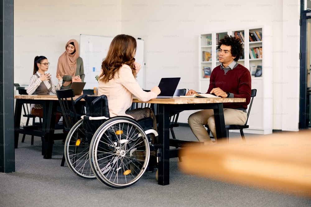 아프리카계 미국인 기업가와 그의 여성 동료가 사무실에서 함께 일하면서 휠체어를 타고 협력하고 있다.