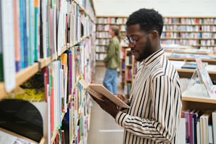 선반 앞에 서서 도서관에서 책을 읽는 아프리카 학생