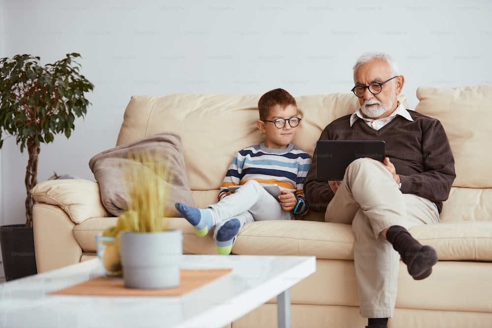 Großvater und Enkel schauen sich zu Hause etwas im Internet auf einem digitalen Tablet an.