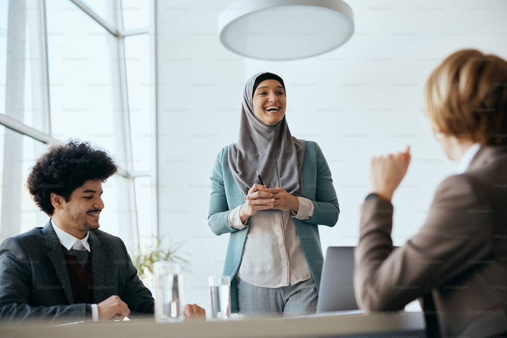Happy Middle Eastern businesswoman communicating with colleagues while leading a meeting at corporate office.