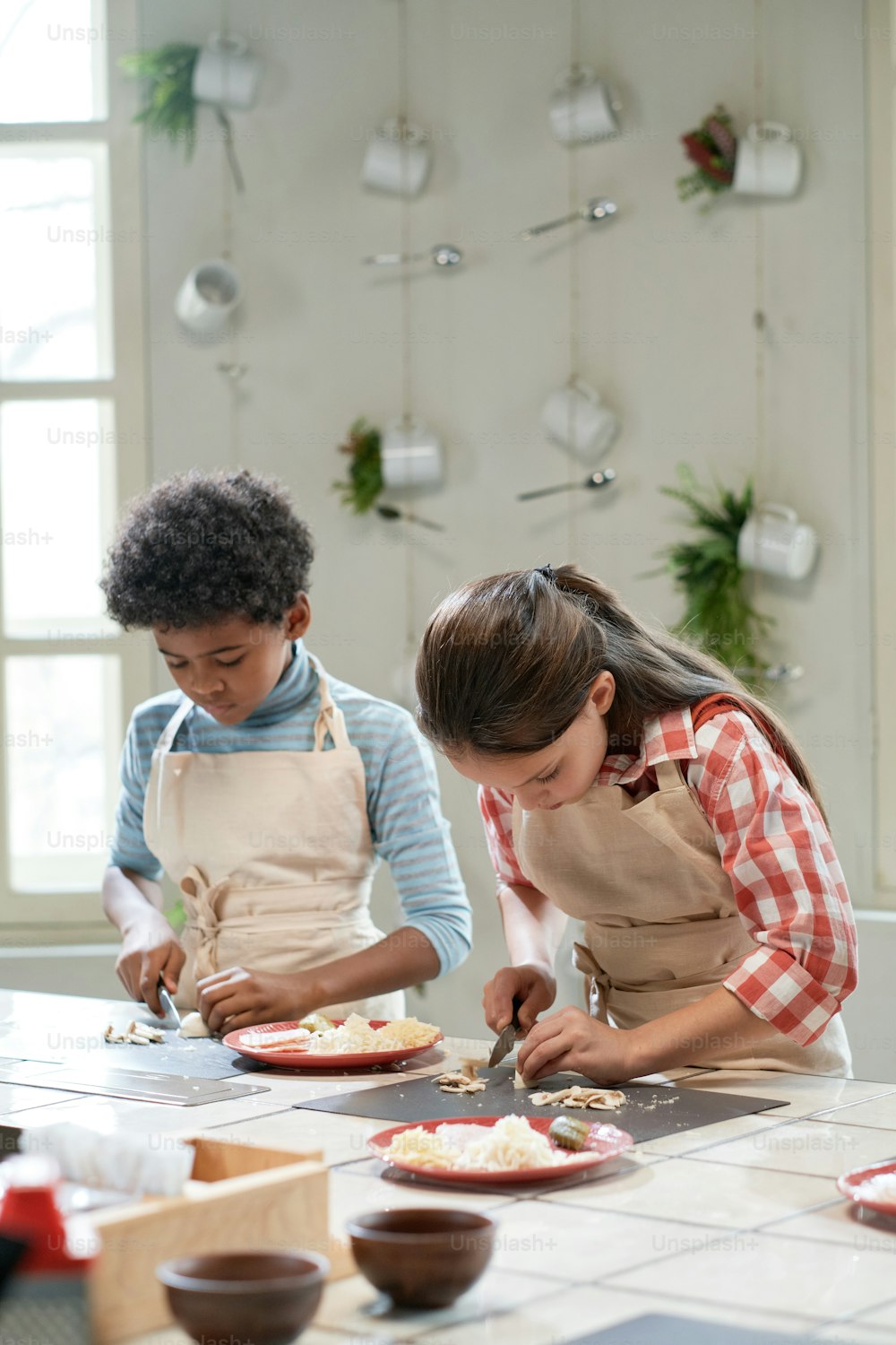 小さな女の子が男の子と一緒にテーブルで野菜を切っていて、キッチンでピザを作っています