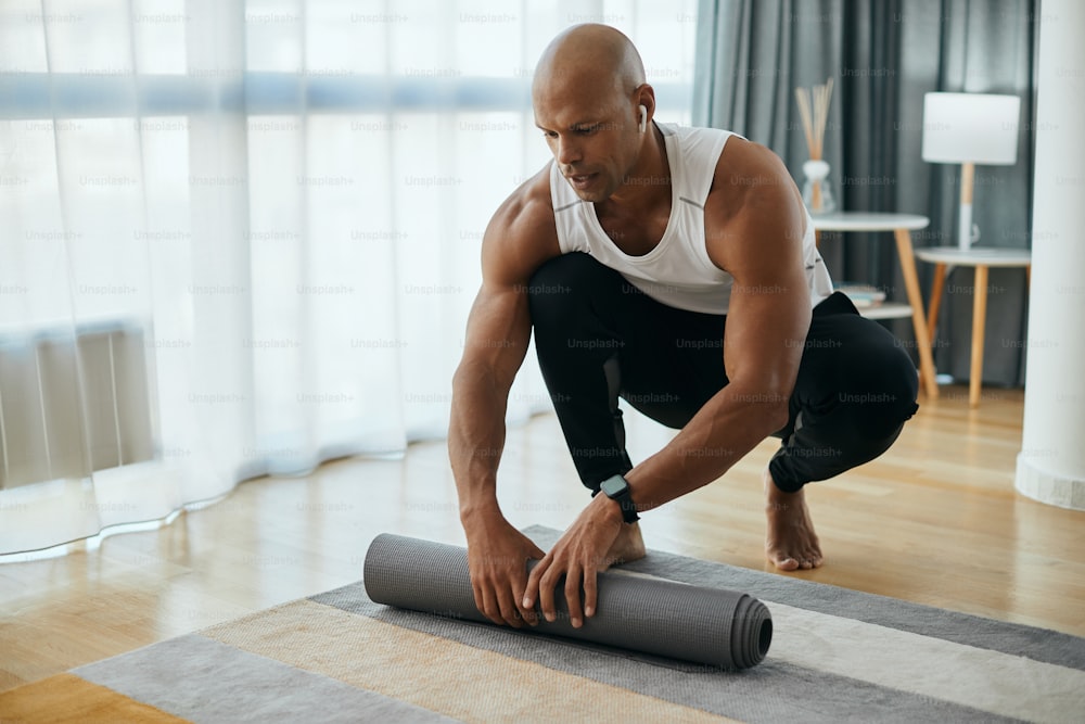 Young African American athletic man rolling up his  exercise mat after working out at home.