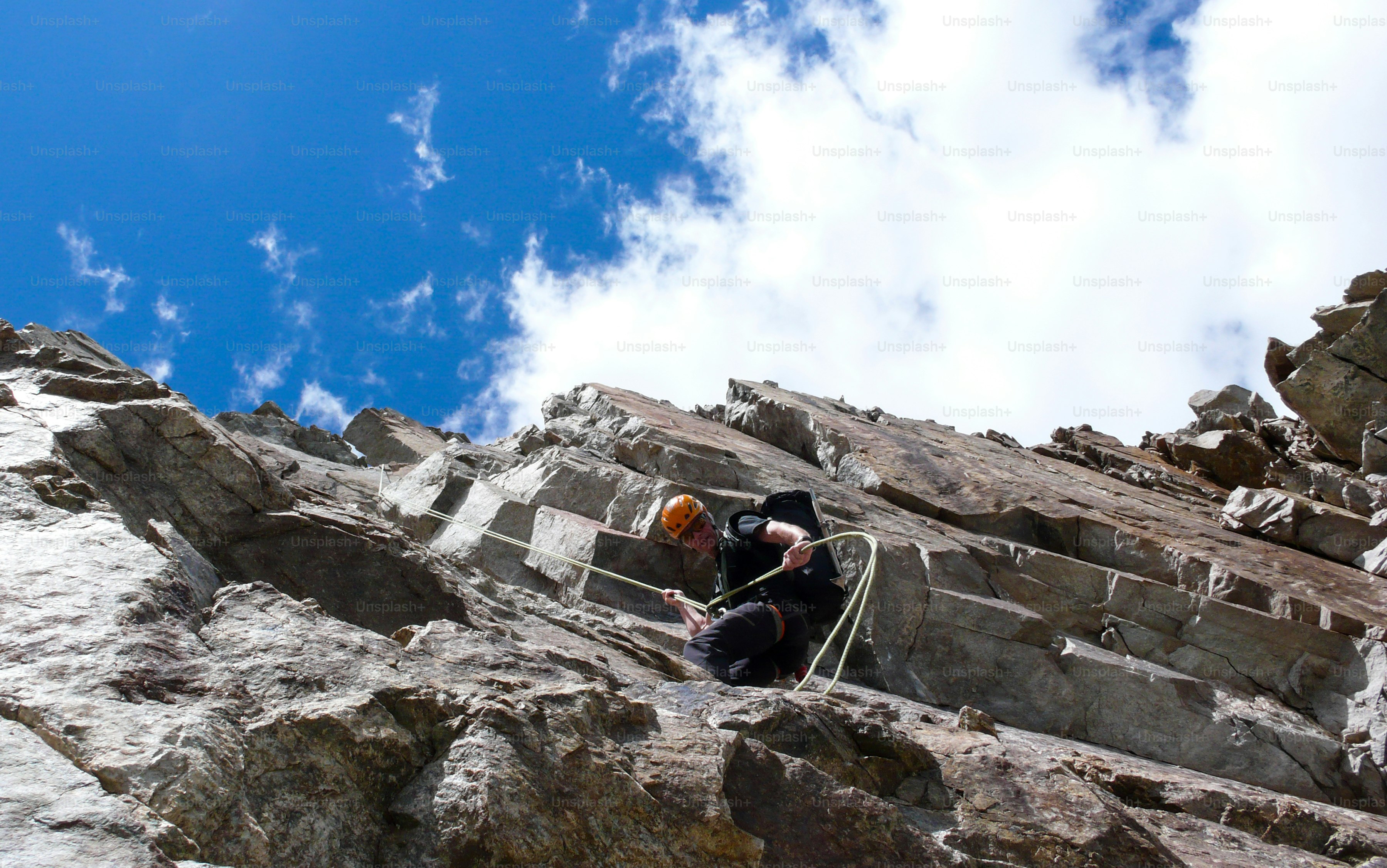 A male mountain guide rappelling off a steep rock face under a