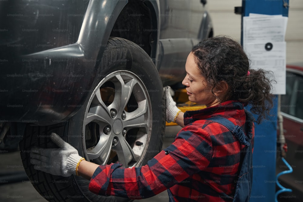Mulher técnica do veículo em luvas de trabalho que muda a roda do automóvel na estação de serviço de reparação