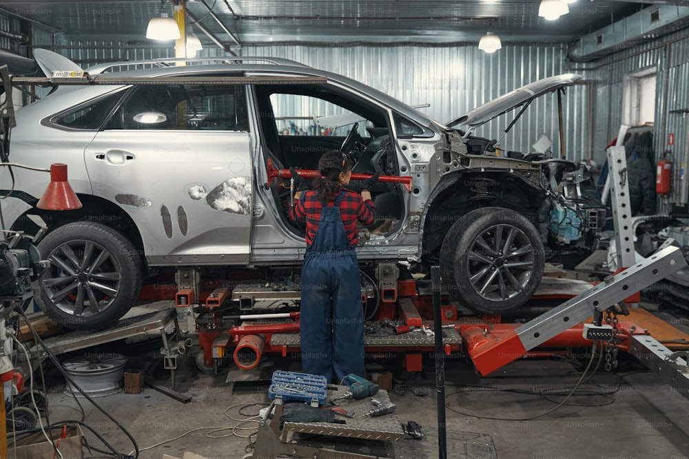 Back view of woman vehicle technician using automotive equipment while fixing automobile in repair service station