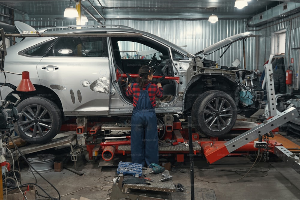 Rückansicht einer Fahrzeugtechnikerin, die Kfz-Ausrüstung benutzt, während sie das Auto in einer Reparaturwerkstatt repariert