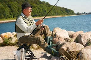 a man sitting on a rock while holding a fishing rod