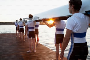 a group of people standing on a dock with a surfboard on their shoulders