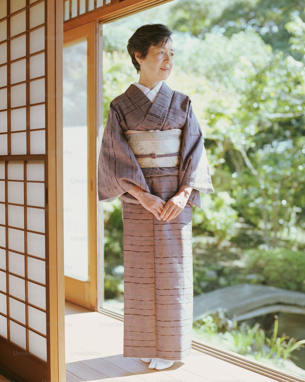 Donna anziana in kimono in piedi nella porta aperta, guardando lontano
