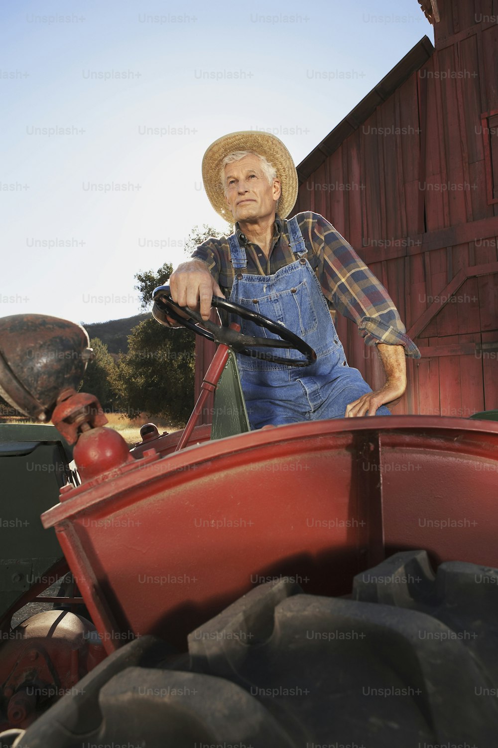 a man in overalls and a straw hat driving a red tractor
