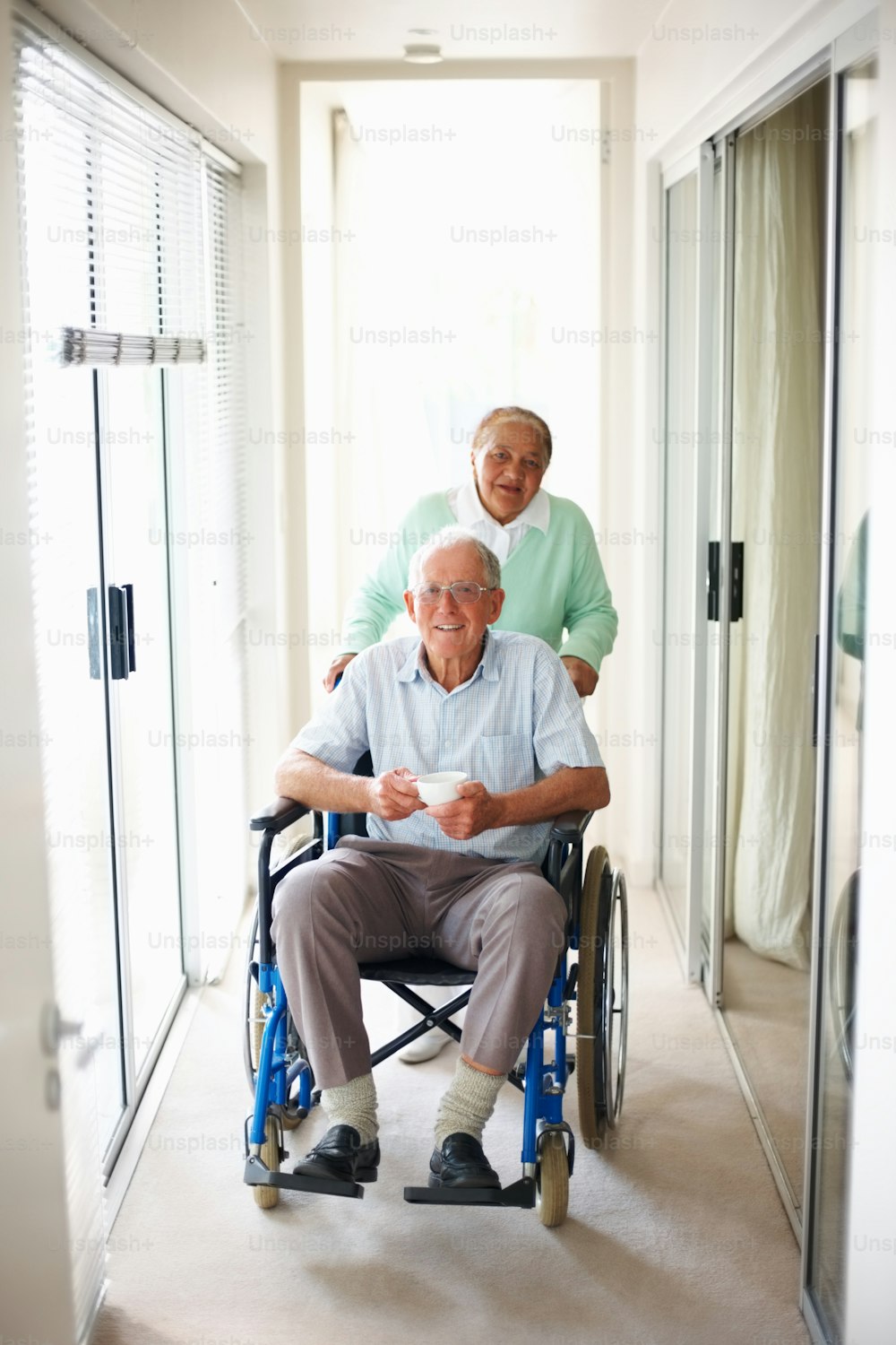 Elderly man on wheelchair assisted by his wife