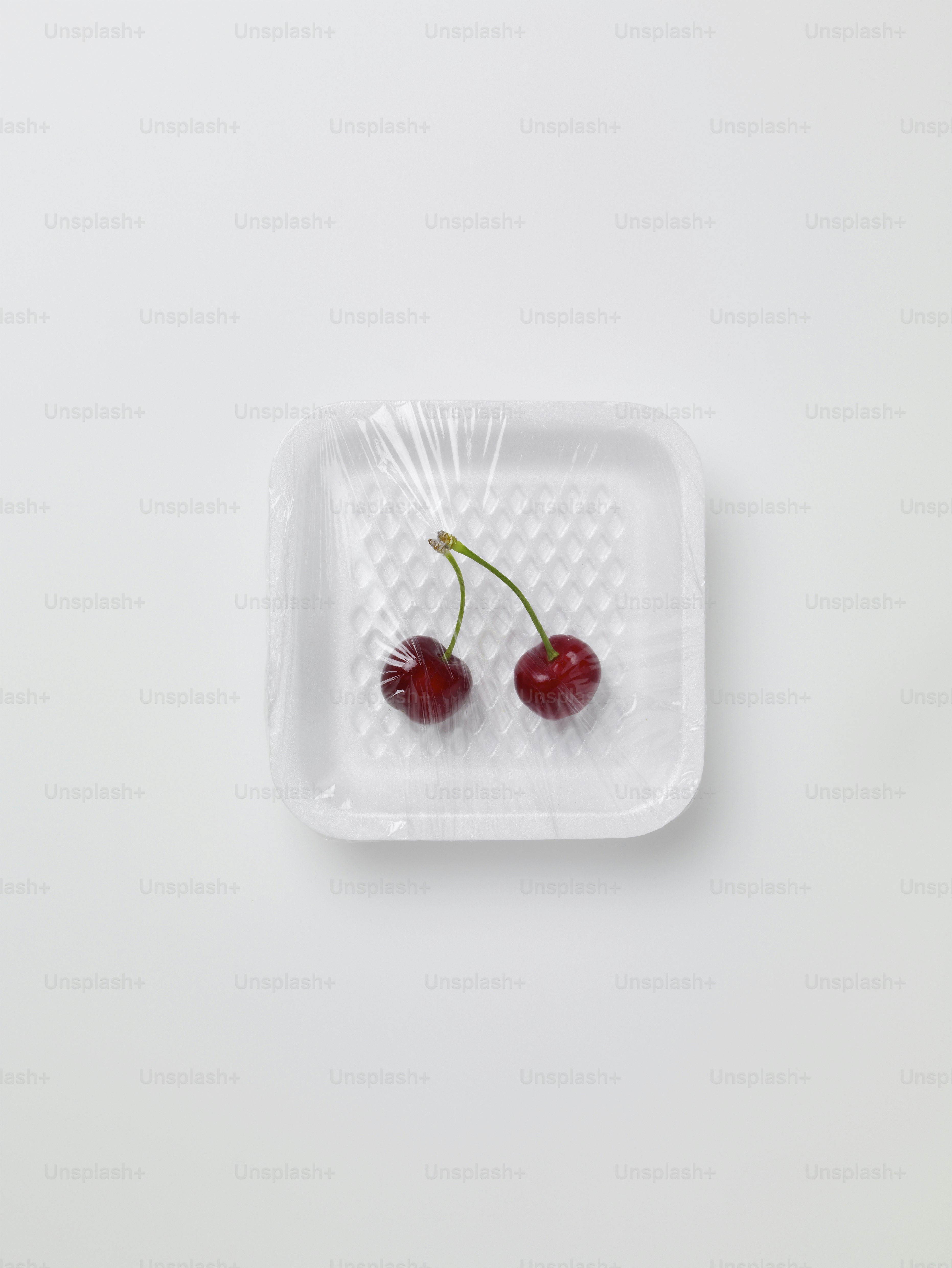 two cherries in a plastic container on a white surface