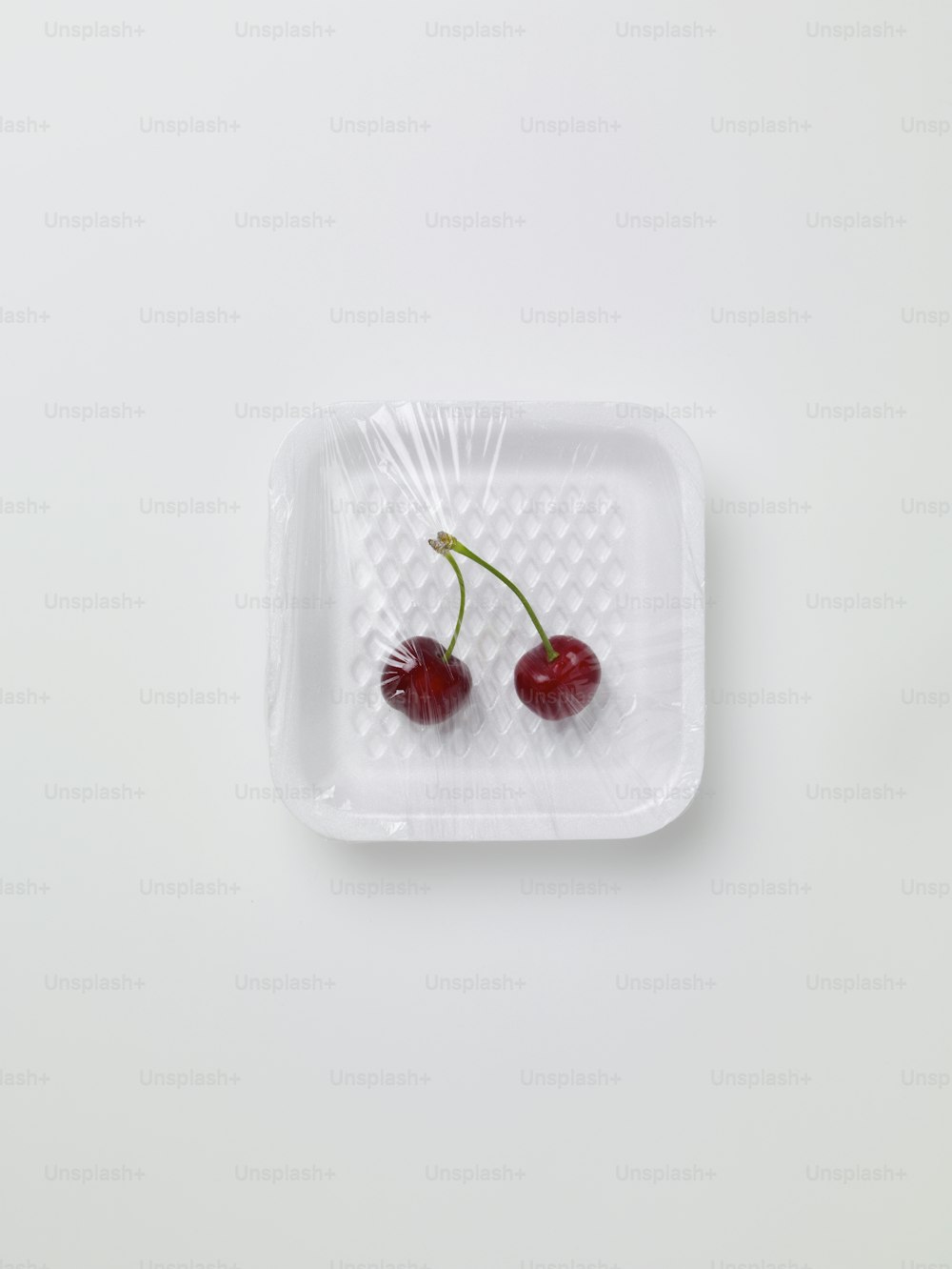 Dos cerezas en un recipiente de plástico sobre una superficie blanca