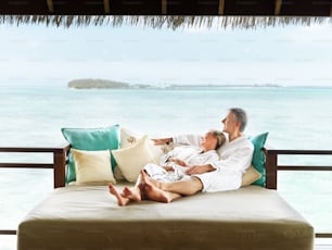 a man and a woman laying on a bed in front of the ocean