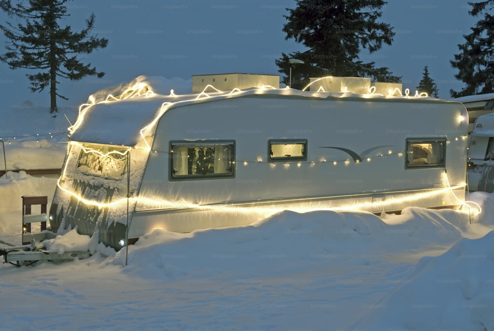 Festive lights decorate a caravan parked in deep snow.
