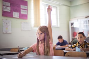 School girl raise hand on class.  Teenagers students sitting in the classroom. Focus is on foreground.