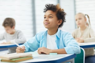 Horizontal potrait of young African American boy sitting at school desk attentively listening to his teacher, copy space