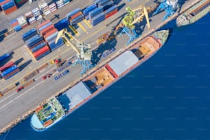 Vista aérea de un enorme buque de carga amarrado en el muelle del puerto, cargando mercancías, metal, hormigón y otras materias primas sólidas