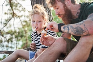 Tasty dinner. Father and daughter camping together. They eating tasty fried marshmallow and chatting with each other. Family concept