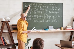 Enseignante debout au tableau noir et pointant du doigt la formule mathématique qu’elle explique aux étudiants à l’université