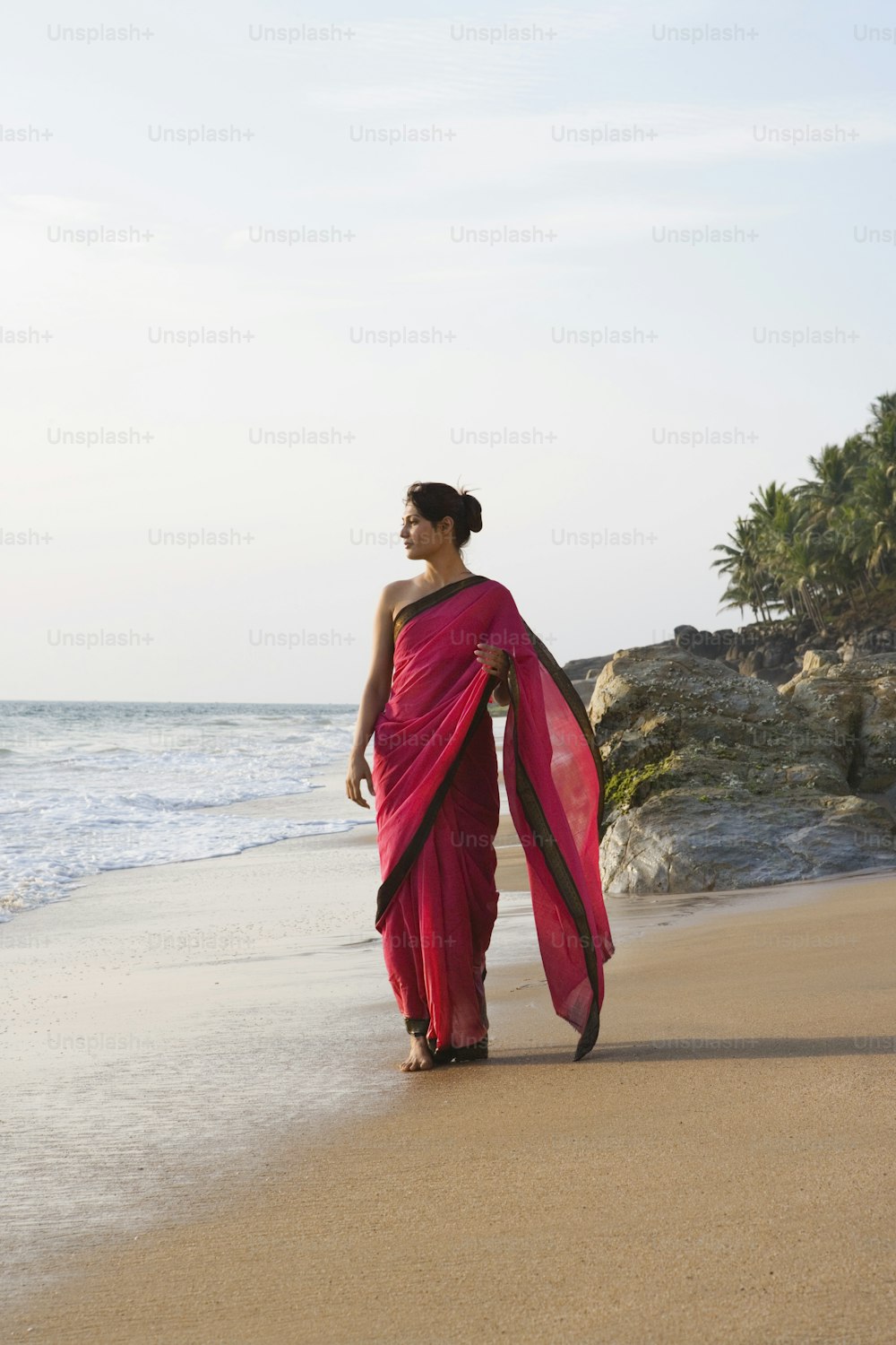 Una donna in un sari rosso che cammina sulla spiaggia