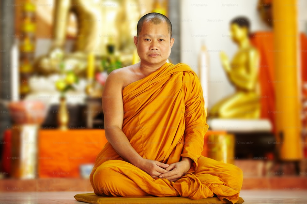 Portrait of a seated monk in a temple wearing a saffron robe and gazing at the camera