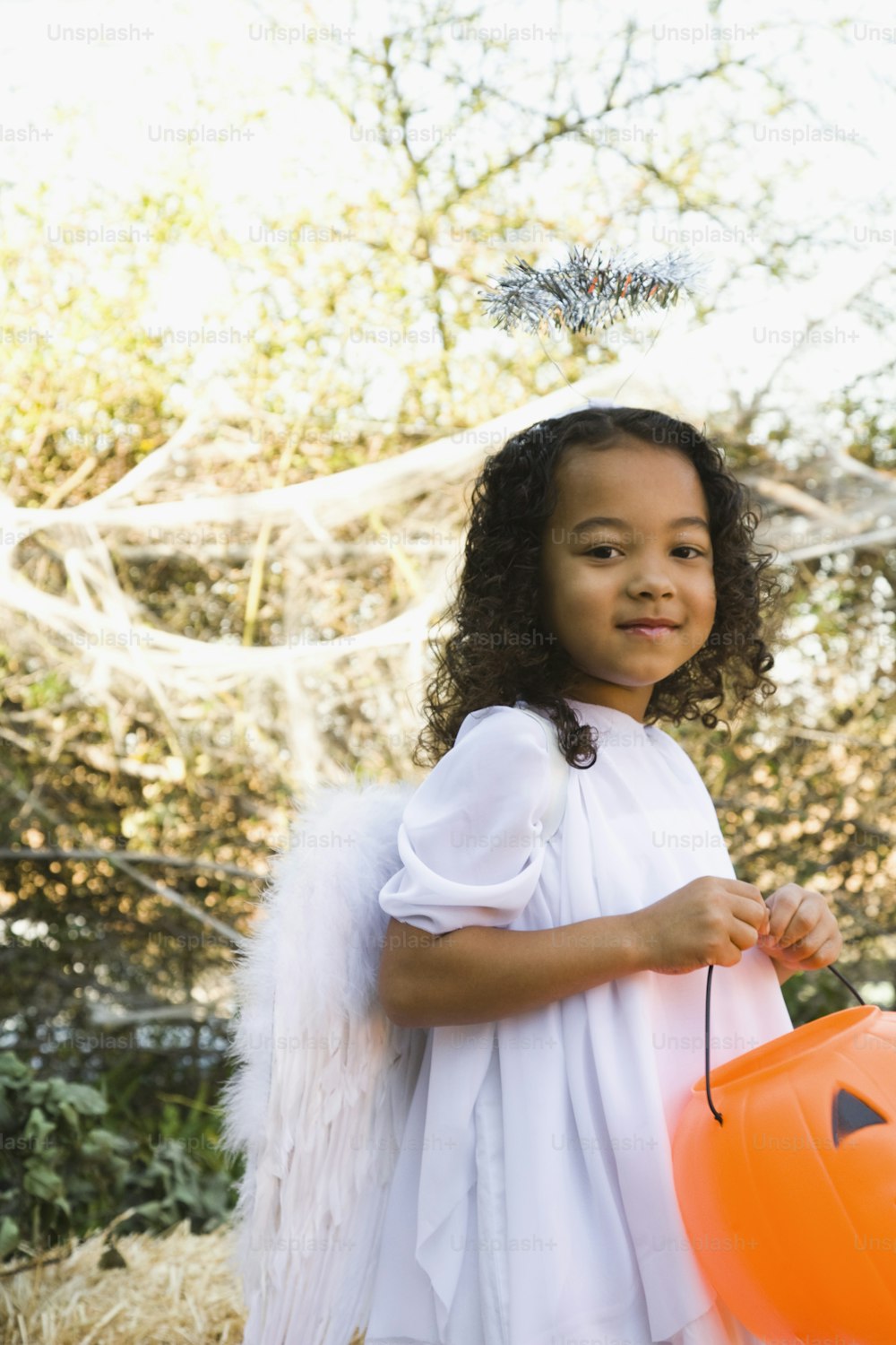 a little girl dressed as an angel holding a pumpkin