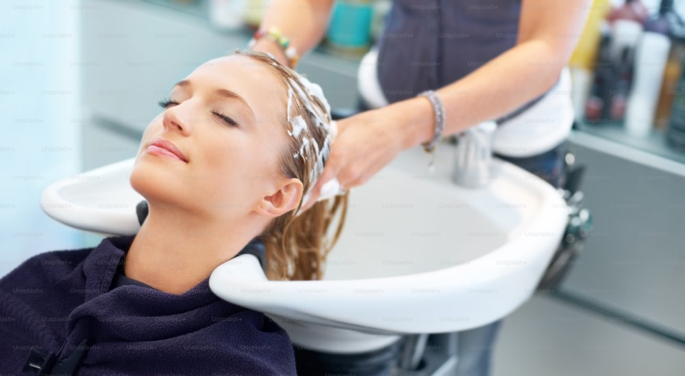 Relaxed young woman leaning back and having her hair washed at the salon