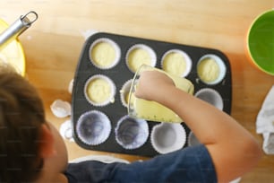 a young boy making cupcakes in a muffin tin
