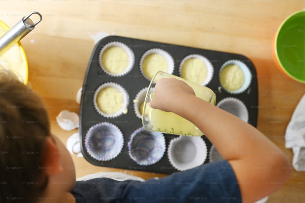 a young boy making cupcakes in a muffin tin