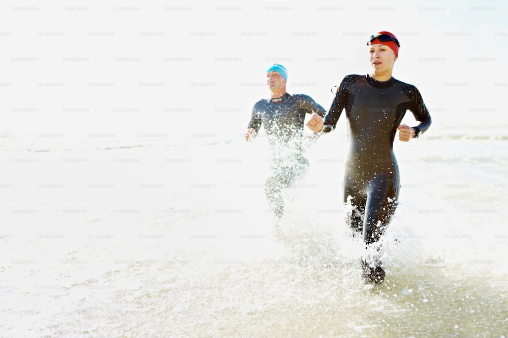 Dos nadadores atléticos saliendo del océano con sus trajes de neopreno puestos