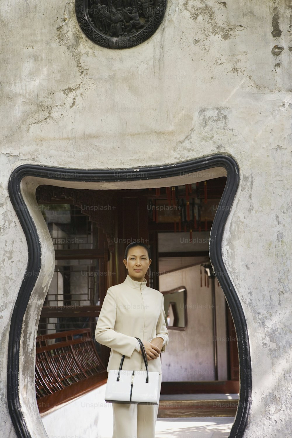 Una mujer parada frente a un espejo sosteniendo un bolso blanco