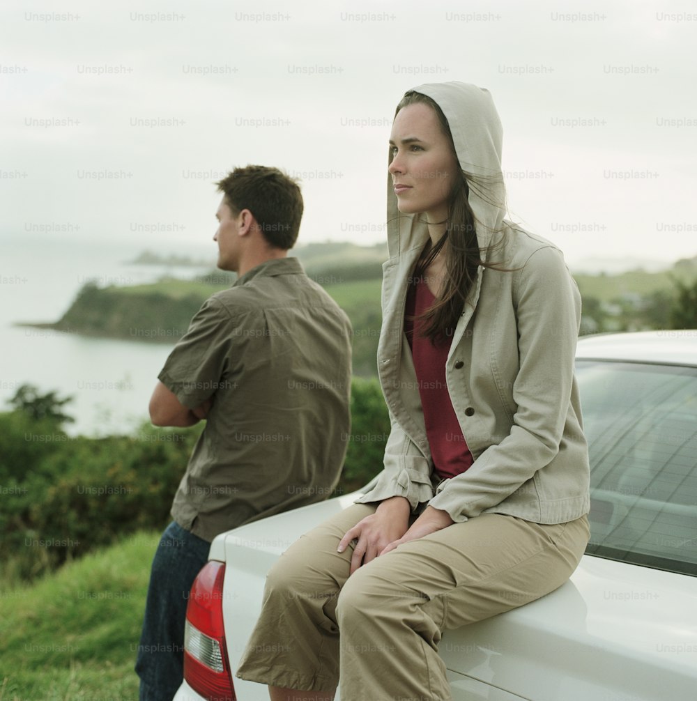海岸線を見ている若いカップル、車の後ろに座っている女性