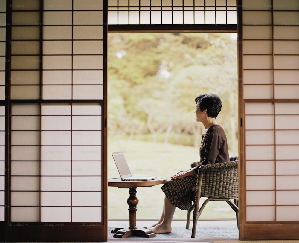 Senior woman sitting beside open doorway, using laptop, side view