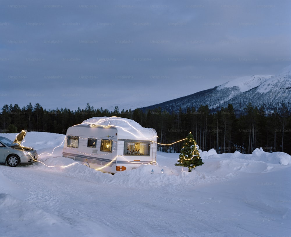 a camper parked in the snow with a christmas tree in front of it